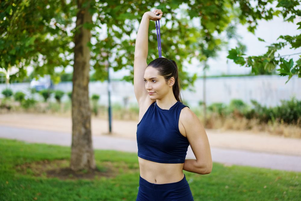 A woman in the park is doing stretching exercises with a resistance band, emphasizing fitness and flexibility