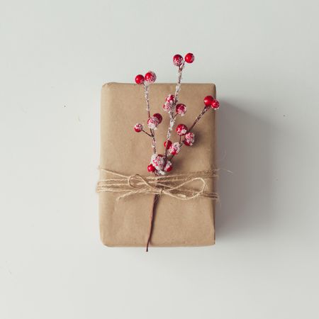 Brown wrapped gift topped with red Christmas berries