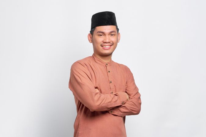 Portrait of Muslim man in kufi head wear smiling with arms crossed