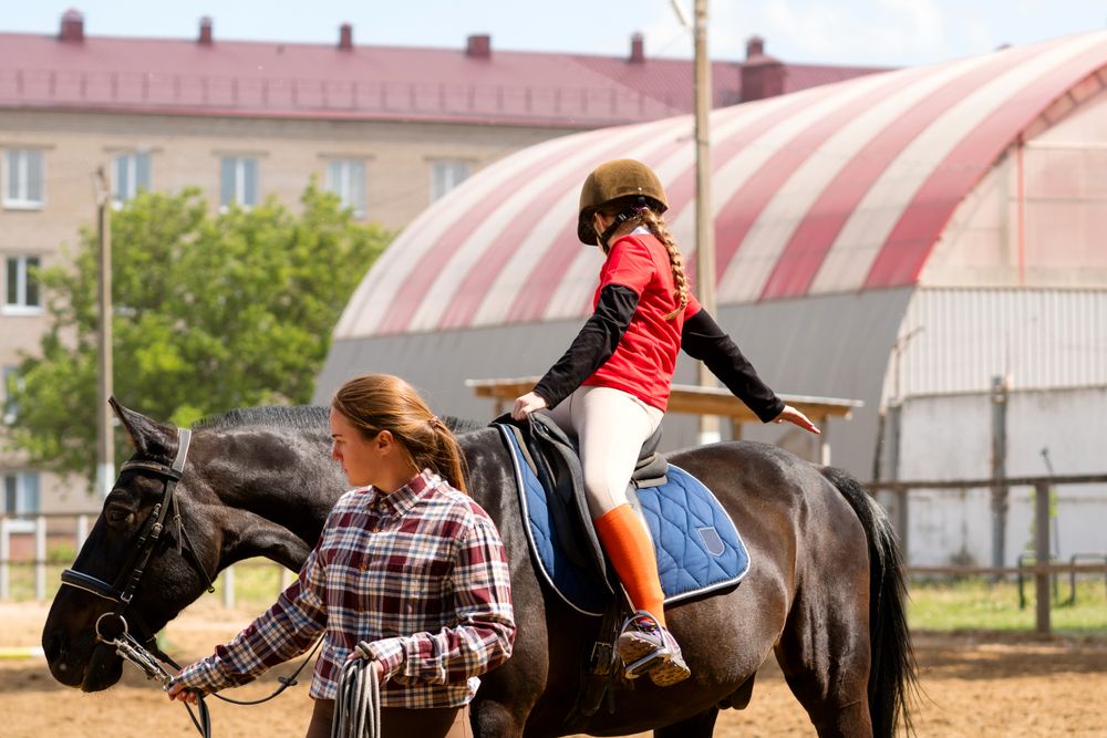Instructor assists young rider during outdoor equestrian session.