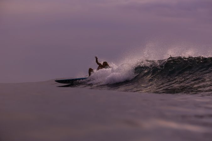 Man on surf board on waving water at sunset