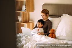 Young mother with her beloved son in the bedroom on the bed watching a movie on laptop bDPMyb