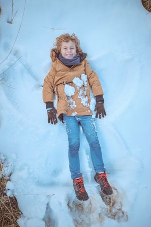 Cheerful boy making snow angel in nature