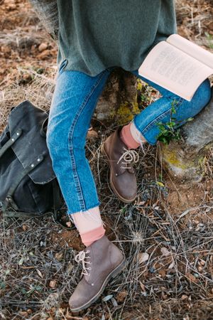 Woman in jeans and boots with book on lap outside