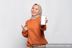 Happy Muslim woman smiling holding smart phone and pointing finger at screen 4je3z5