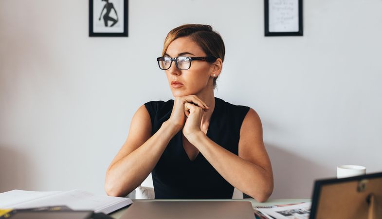 Woman wearing glasses sitting at her desk in office looking away