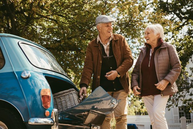Older couple putting picnic basket in the trunk of their vintage car