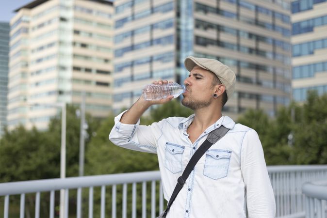 Male on bridge with city in background sipping water