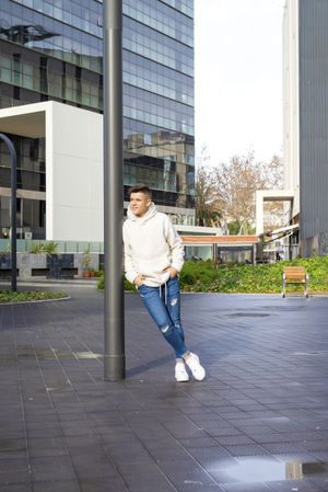 Portrait of young adult with hands in pocket leaning on pole outside