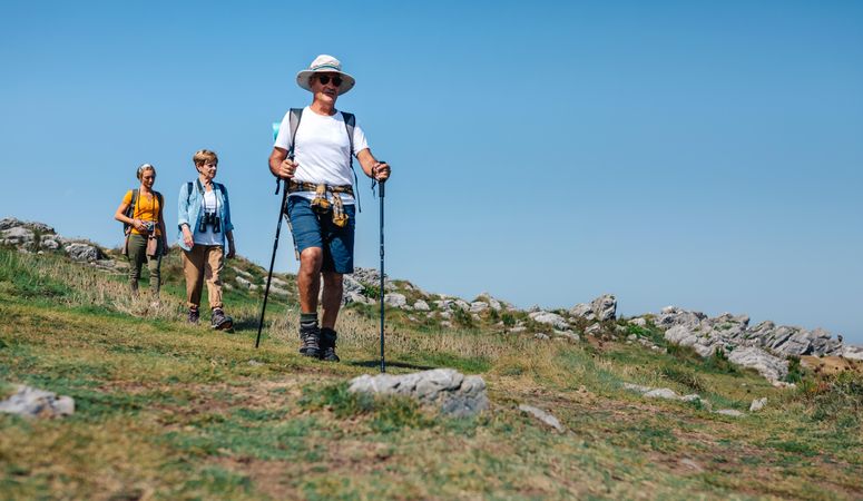 Mature adults with daughter hiking on hill with poles