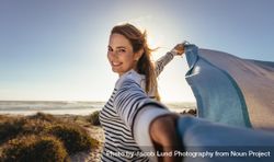 Portrait of a smiling woman holding a drape against the sea breeze 4Zl7x0
