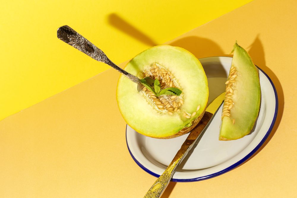 Sliced small melon on plate with spoon and fork