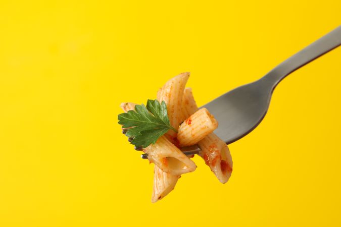 Fork with tasty pasta on yellow background, close up