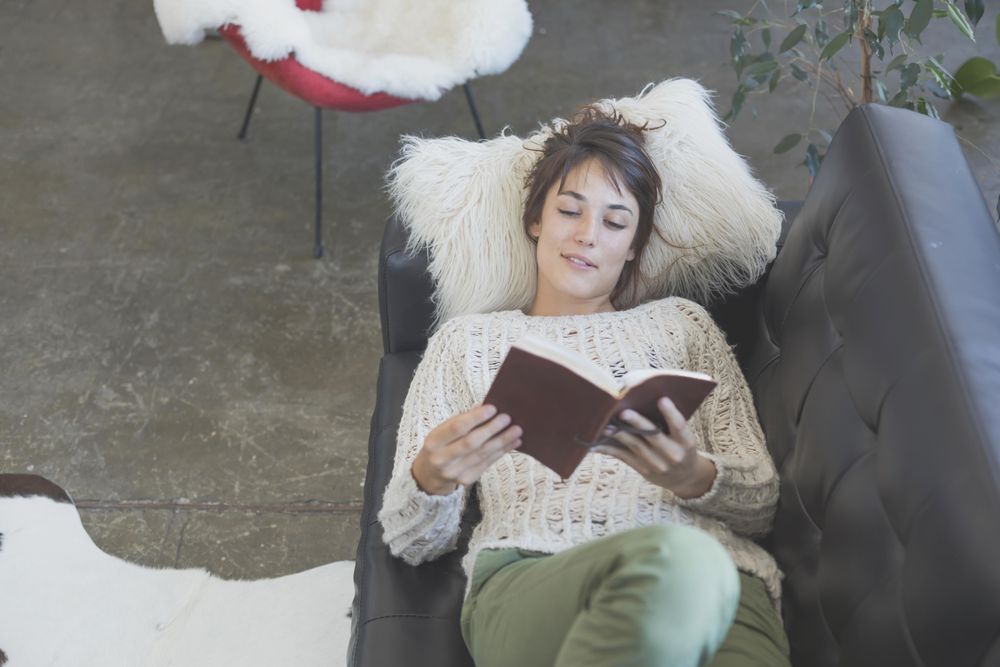 Looking down at female lying back and reading on leather sofa
