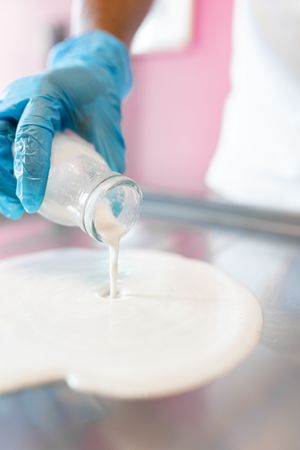 A worker is dropping milk with a jar on a rolled ice cream machine