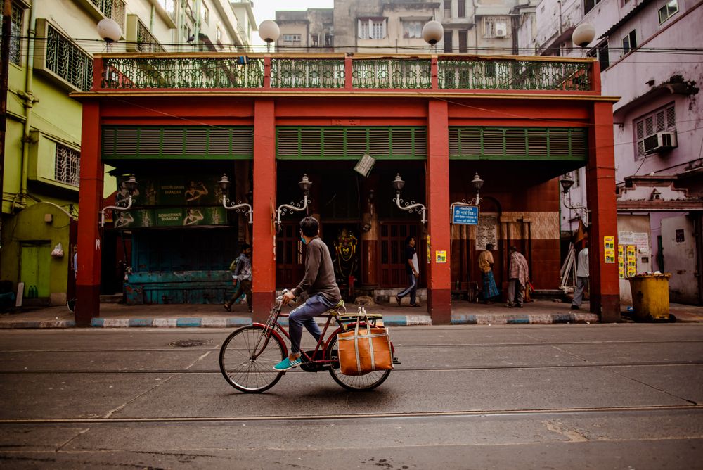 Side view of a man riding a bicycle on the road beside a red building