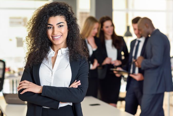 Curly haired businesswoman standing in foreground of busy office
