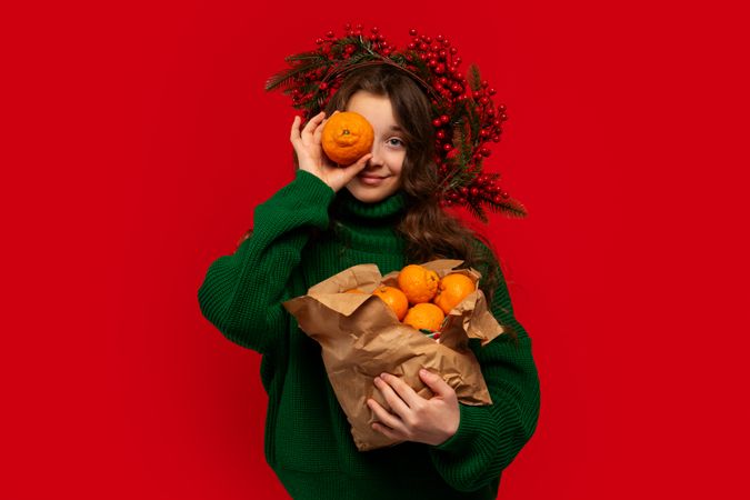Young girl in green sweater holding paper bag of oranges