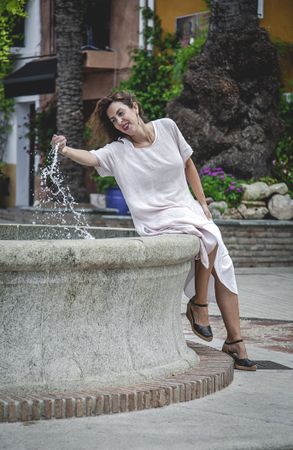 Joyful female splashing water in city fountain