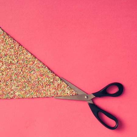 Scissors with sprinkles on pink background