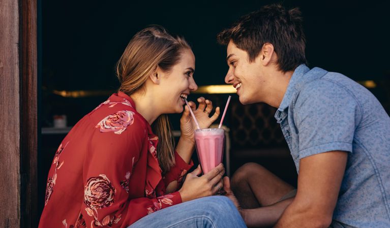 Couple on a date and enjoying a milkshake with two straws looking at each other