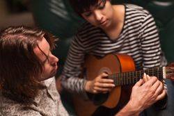 Young Musician Teaches Female Student To Play the Guitar