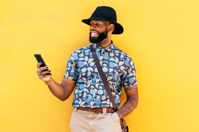 Stylish Black man using smartphone outdoors over yellow background