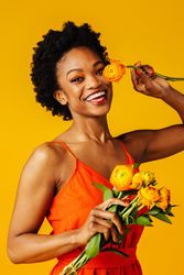 Joyful Black woman playing with ranunculus flowers