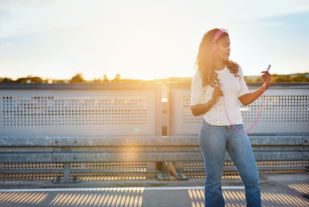 Woman standing on rooftop in pink headphones looking at her phone