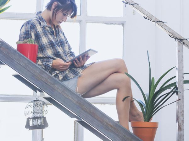 Side view of female in flannel shirt lounging at home with digital tablet