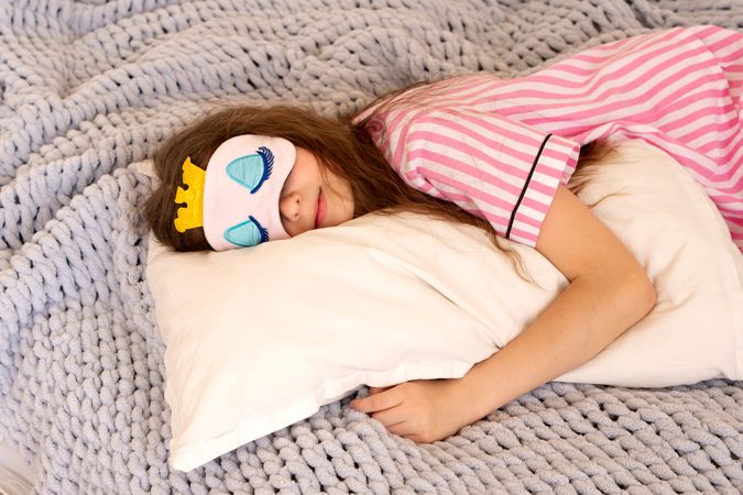 Girl sleeping with sleep mask on cozy knitted blanket.
