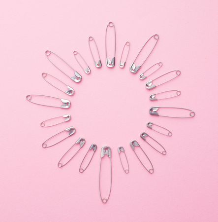 Safety pins in a circle shape over pink background