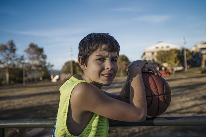 Young teen male with sleeveless shirt standing on a street basket court while smiling at camera