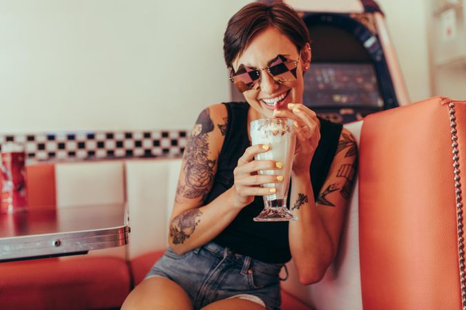 Woman with tattooed arms drinking milkshake sitting at a restaurant