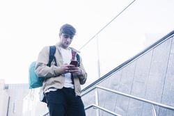 Man walking down stairs with backpack while using mobile outdoors