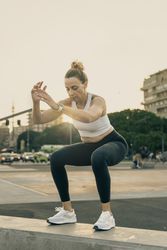 Athletic woman landing a box jump or doing a squat during an outdoor HIIT workout