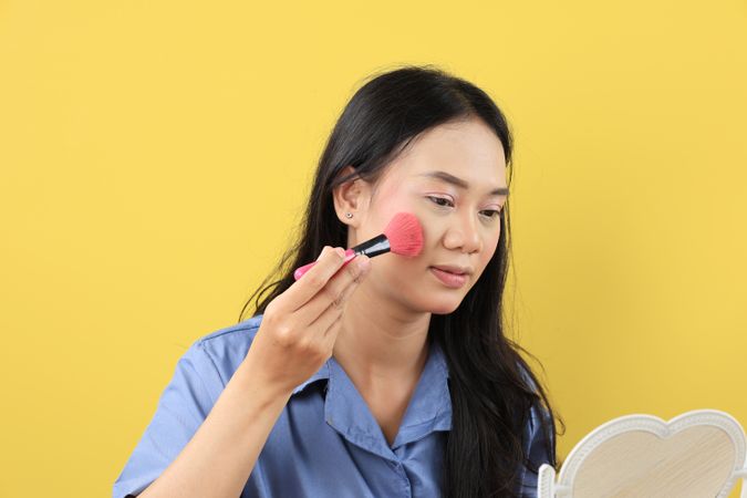 Young Asian Woman Holding Pink Makeup Brush,  Apply Blush on or Higlighter to the Cheek.
