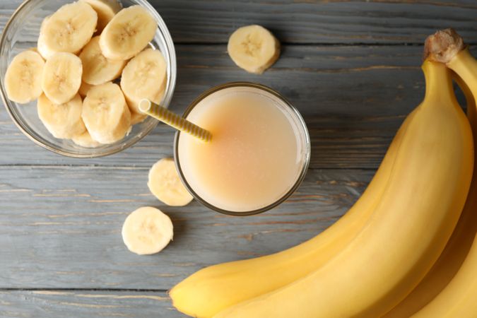 Bananas and juice on wooden background, top view