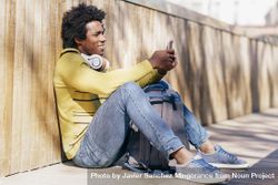 Man sitting against wall outside and smiling while checking phone bxDprb