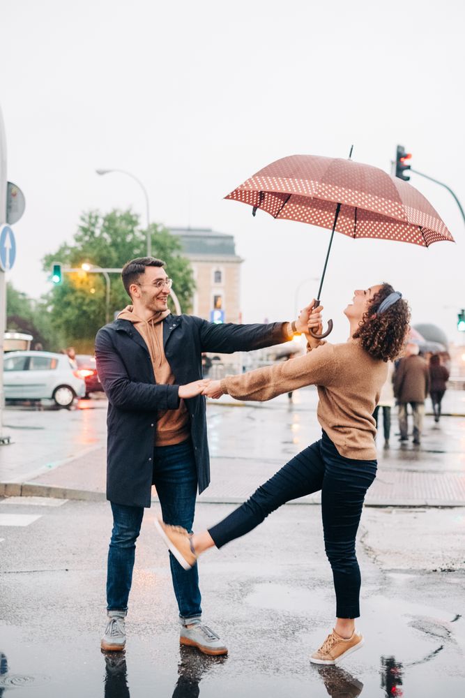 Happy couple with umbrella hugging on wet street