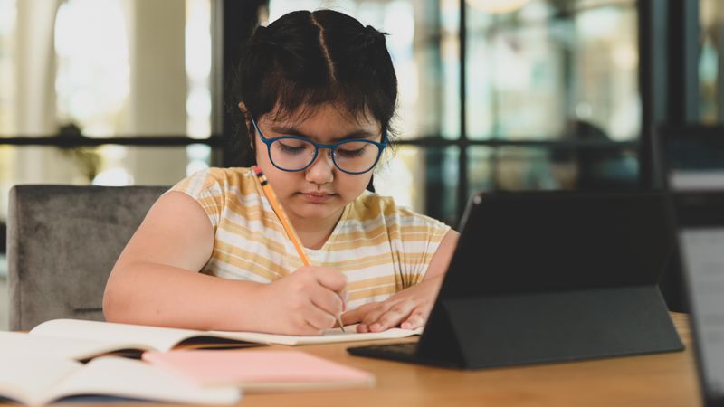 Asian child girl wearing glasses writing in notebook