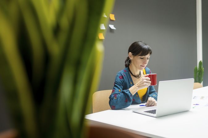 Businesswoman with hot beverage using laptop