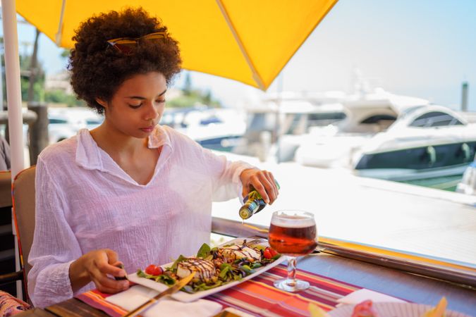 Woman putting olive oil on salad in waterfront cafe