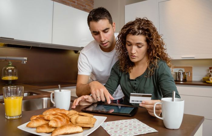 Man and woman having breakfast in kitchen while buying something on tablet