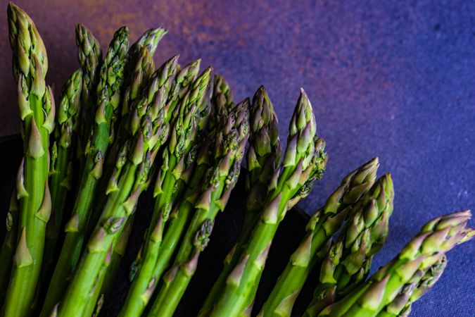 Row of raw asparagus tips on blue marble background