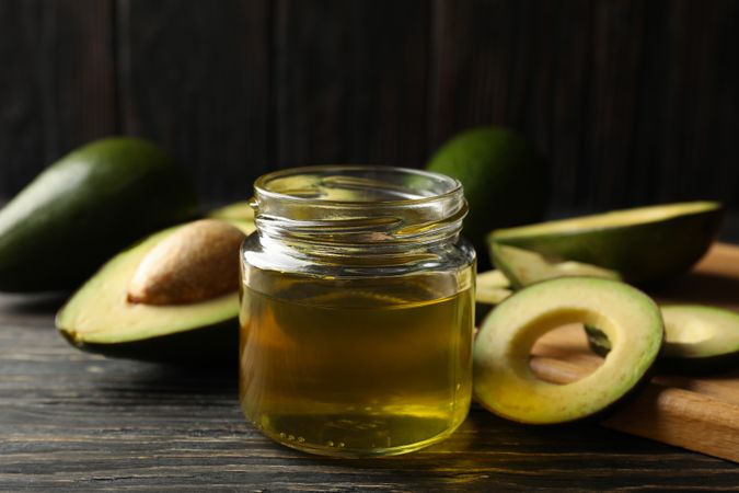 Board, avocado and oil on wooden background, close up