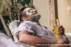 Relaxed man sitting on chair with facial mask on face holding a glass of juice bYGGg5