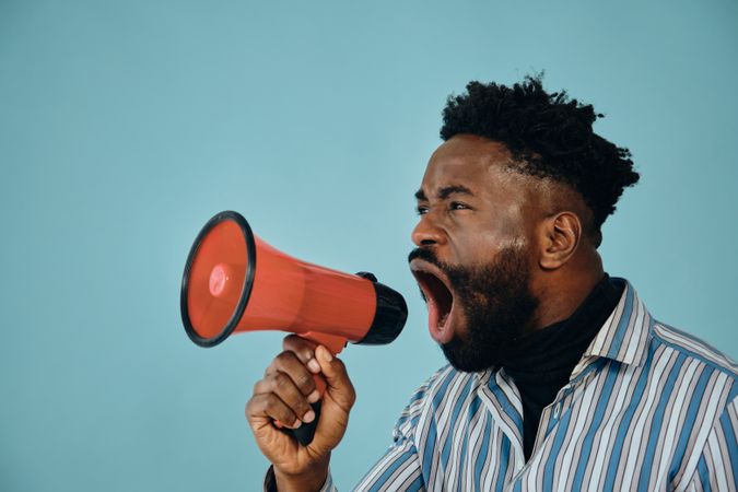Portrait of a Black man in blue studio shoot screaming into megaphone