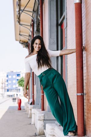 smiling young woman hanging on a pole in the street while looking camera
