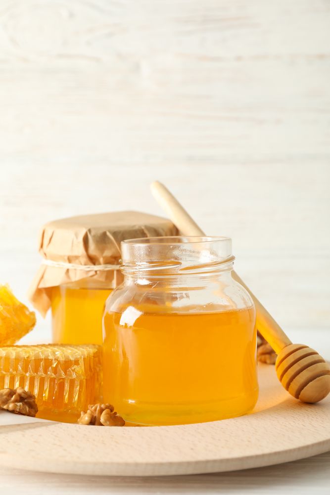 Honeycombs, walnuts, dipper and jars with honey on wooden background, copy space